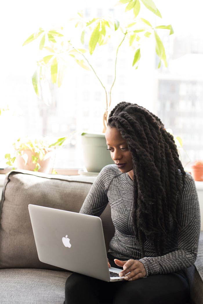Black woman with dreadlocks using a laptop indoors, embodying modern remote work lifestyle.