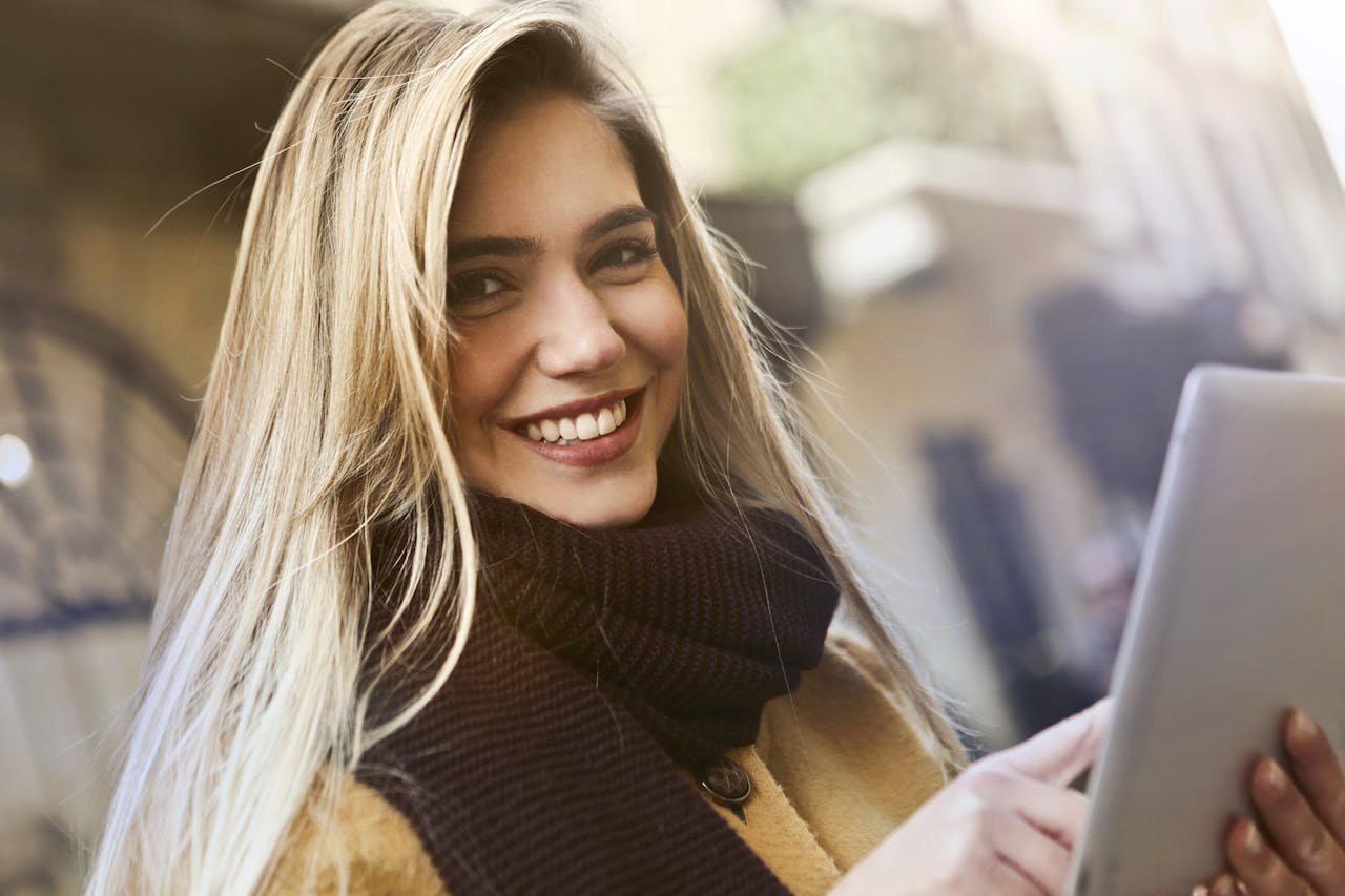Smiling woman holding a tablet outdoors, captured in natural lighting. Ideal for technology and lifestyle themes.