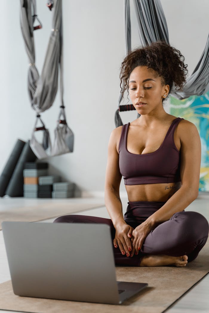 Woman practicing meditation and yoga indoors with online guidance, focusing on relaxation.