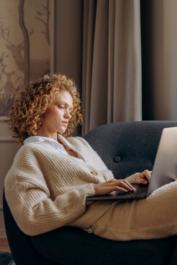 A relaxed woman with curly hair working on a laptop in a cozy home setting.