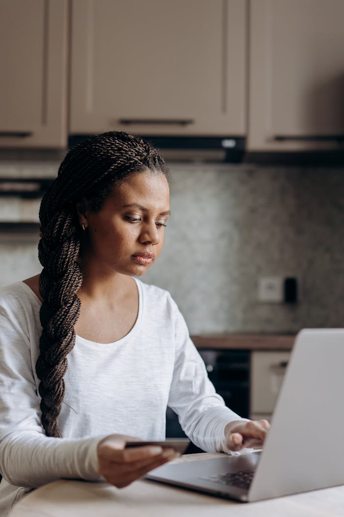 Woman holding credit card and using laptop for online shopping at home.