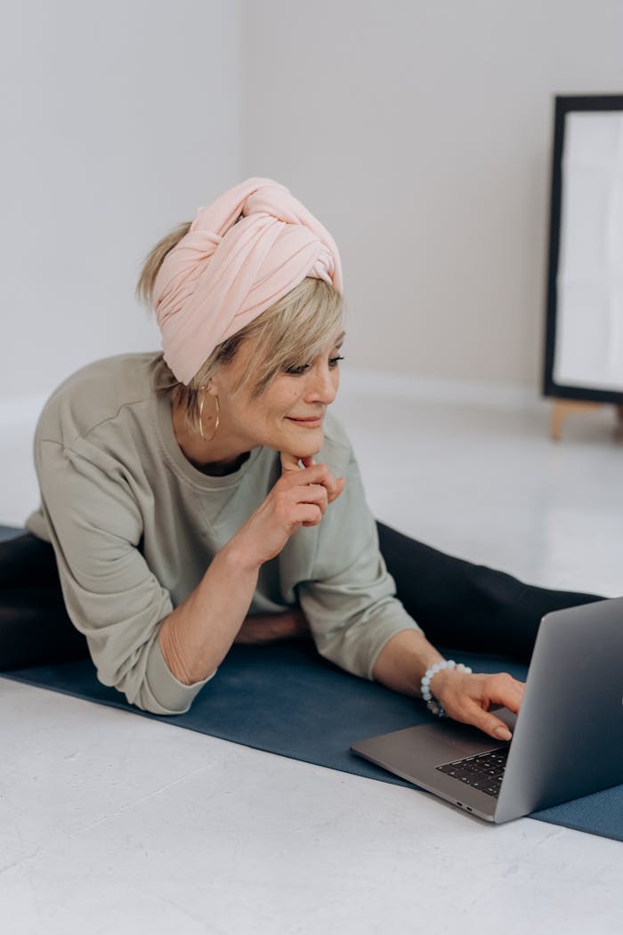 Woman relaxing on a yoga mat at home, using a laptop for leisure or work activities.